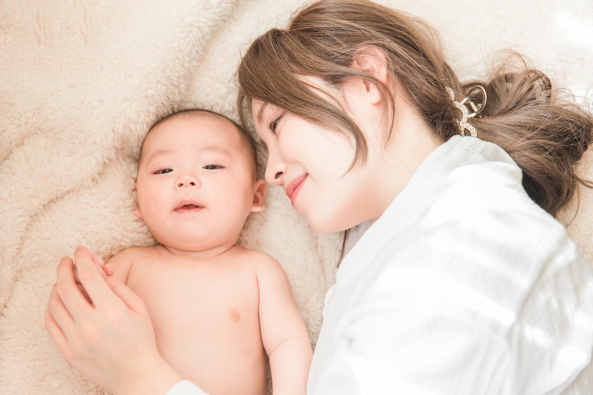 赤ちゃんと寄り添って布団で寝ているお母さんの写真